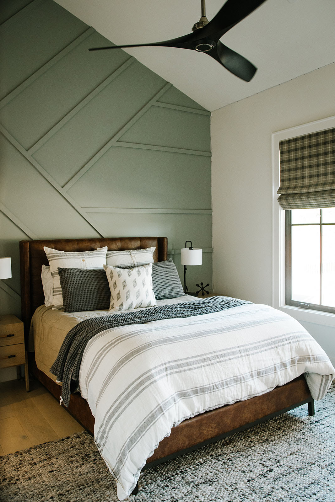 Cozy Modern Bedroom with Accent Wall and Leather Bed Frame – A beautifully designed bedroom with a geometric accent wall, plaid Roman shades, and a tufted leather bed, combining rustic charm with modern interior design elements.