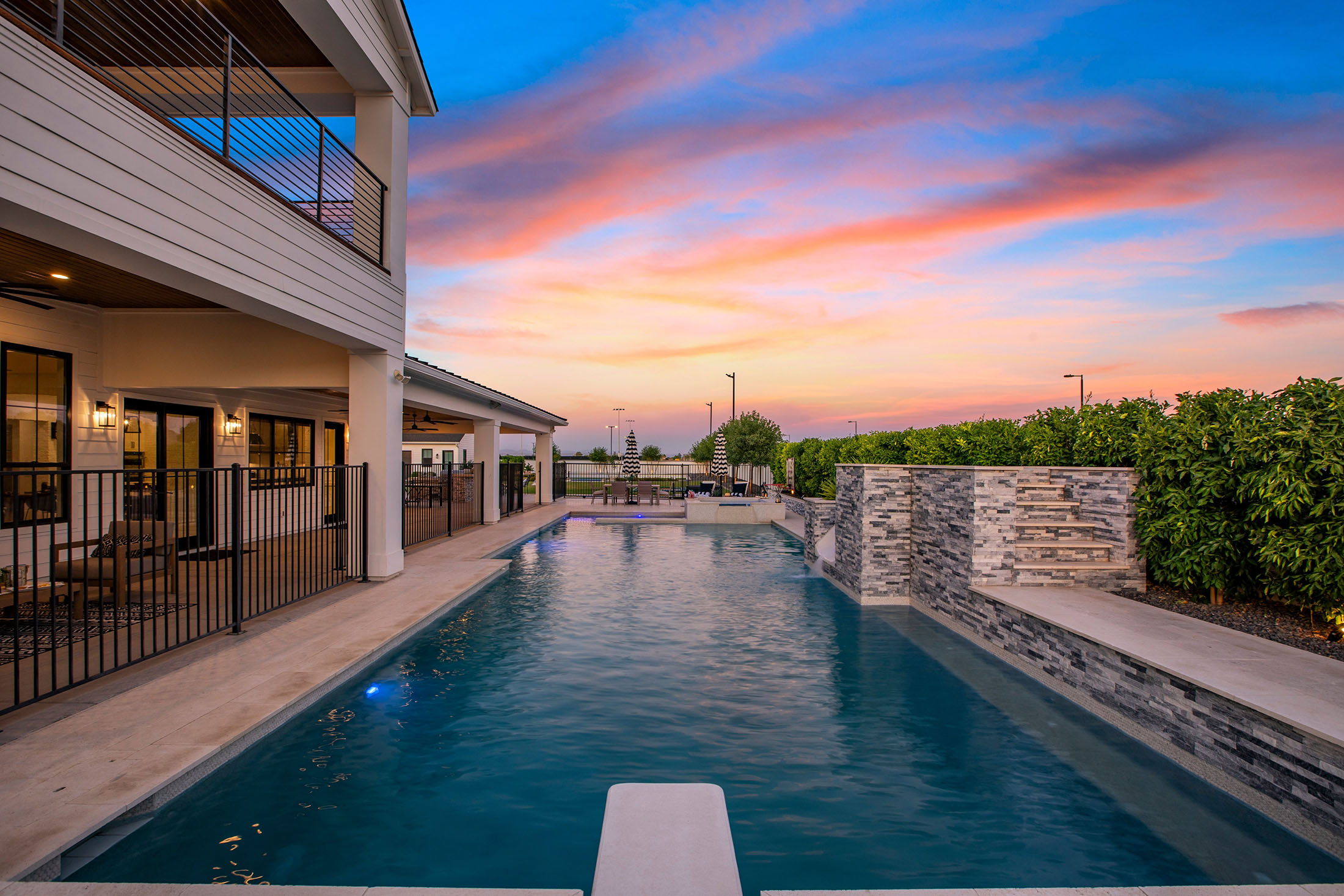 Luxury backyard pool with sunset view and stone waterfall – A breathtaking outdoor space with a resort-style pool, stone waterfall, and lush greenery, set against a picturesque sunset sky.