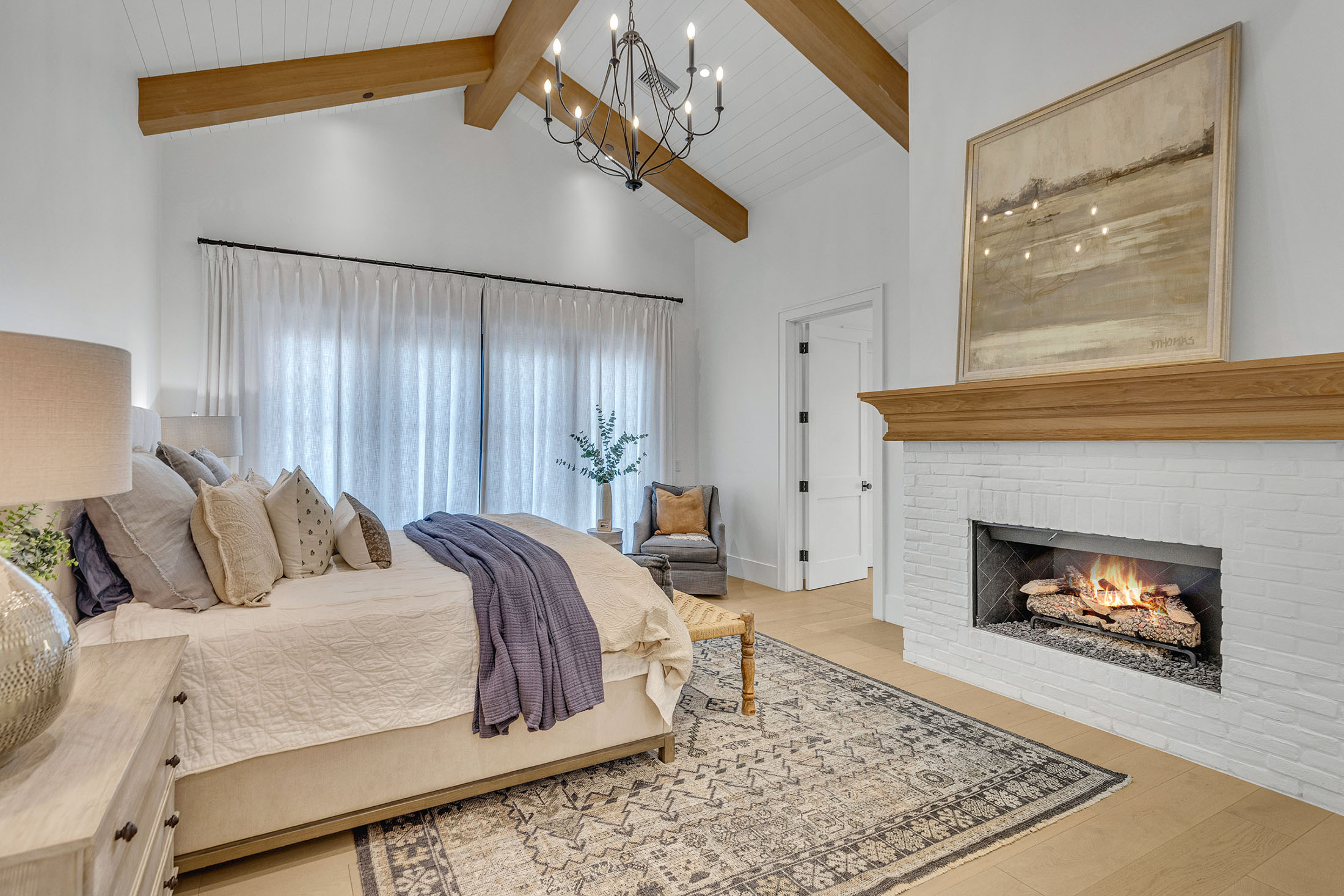 Serene master bedroom with vaulted wood-beamed ceilings, a fireplace, and luxurious neutral decor.