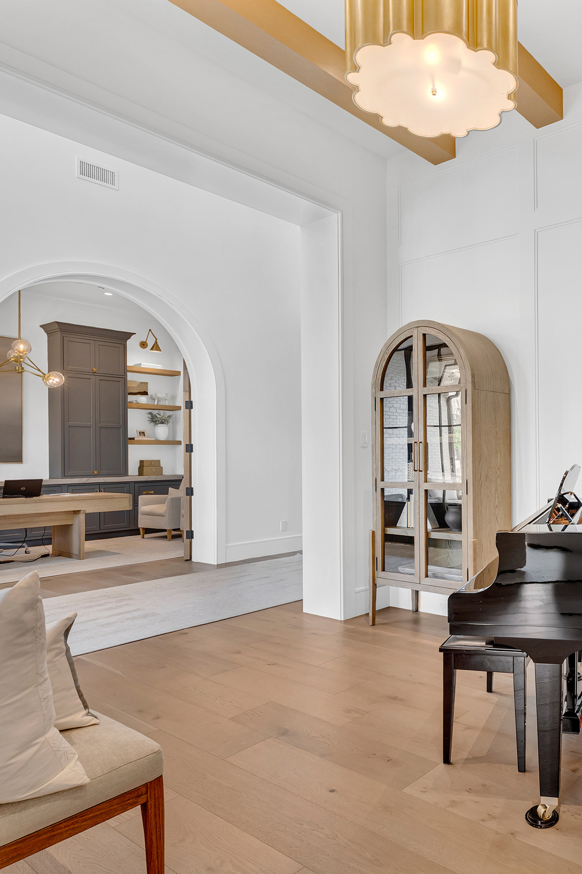 Sophisticated Home Office with Arched Doorway - A stylish home office with a natural wood desk, plush white armchairs, dark cabinetry, and floating shelves, framed by a striking arched entryway.