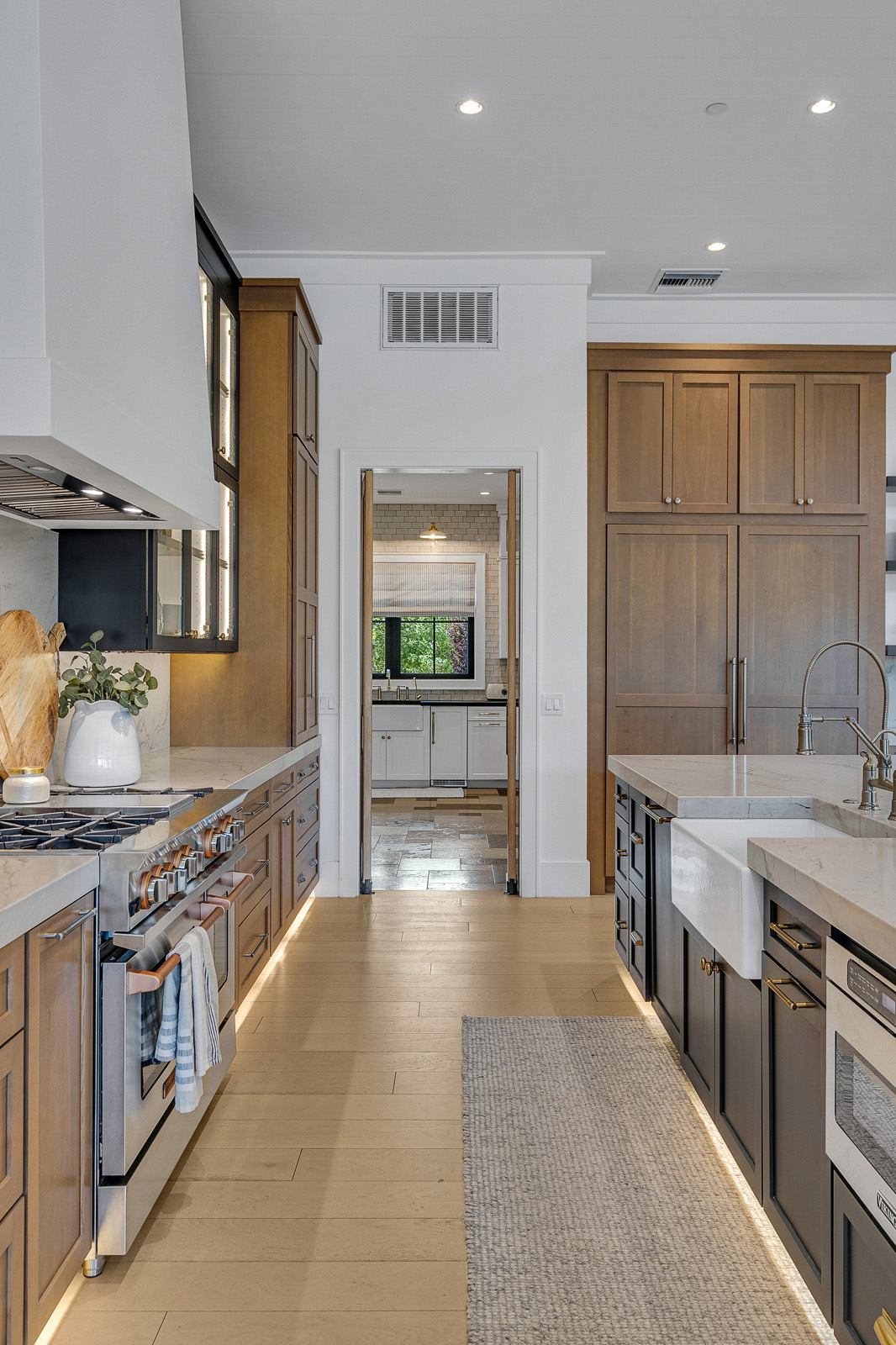 Gourmet Kitchen with Professional Appliances and Custom Wood Finishes – A stylish chef’s kitchen with high-end appliances, black and wood cabinetry, a farmhouse sink, and an elegant marble backsplash for a sophisticated, functional space.