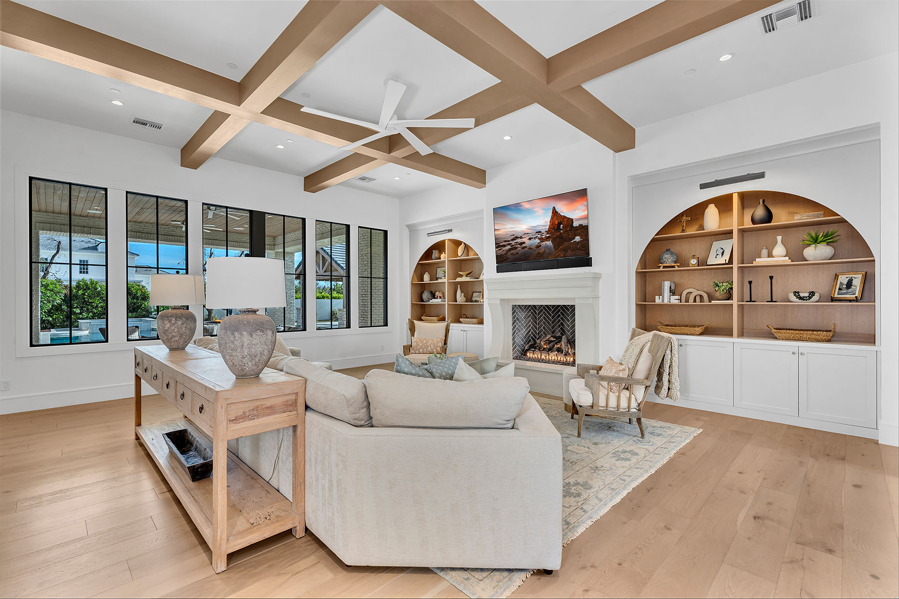Elegant Living Room with Fireplace and Built-In Arch Shelves – A cozy yet sophisticated living room featuring a white fireplace, arched built-in shelves with decorative elements, and a plush neutral-toned sectional. Wooden ceiling beams add a rustic charm.