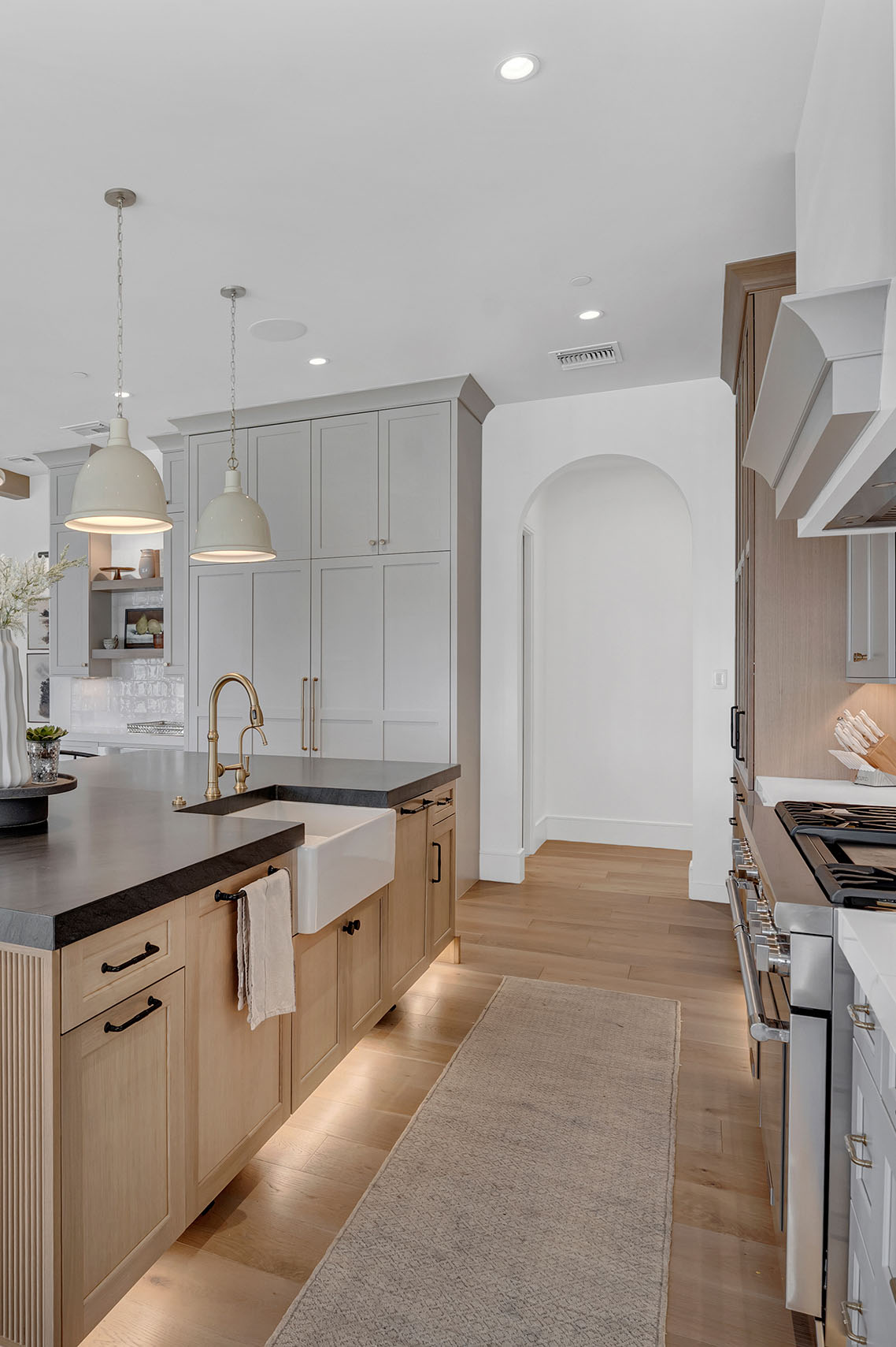 Stunning kitchen featuring a black quartz island, white shaker cabinets, and a built-in glass-front display for dinnerware. Soft gold pendant lights and brass hardware complement the warm wood tones, blending elegance with modern farmhouse charm.