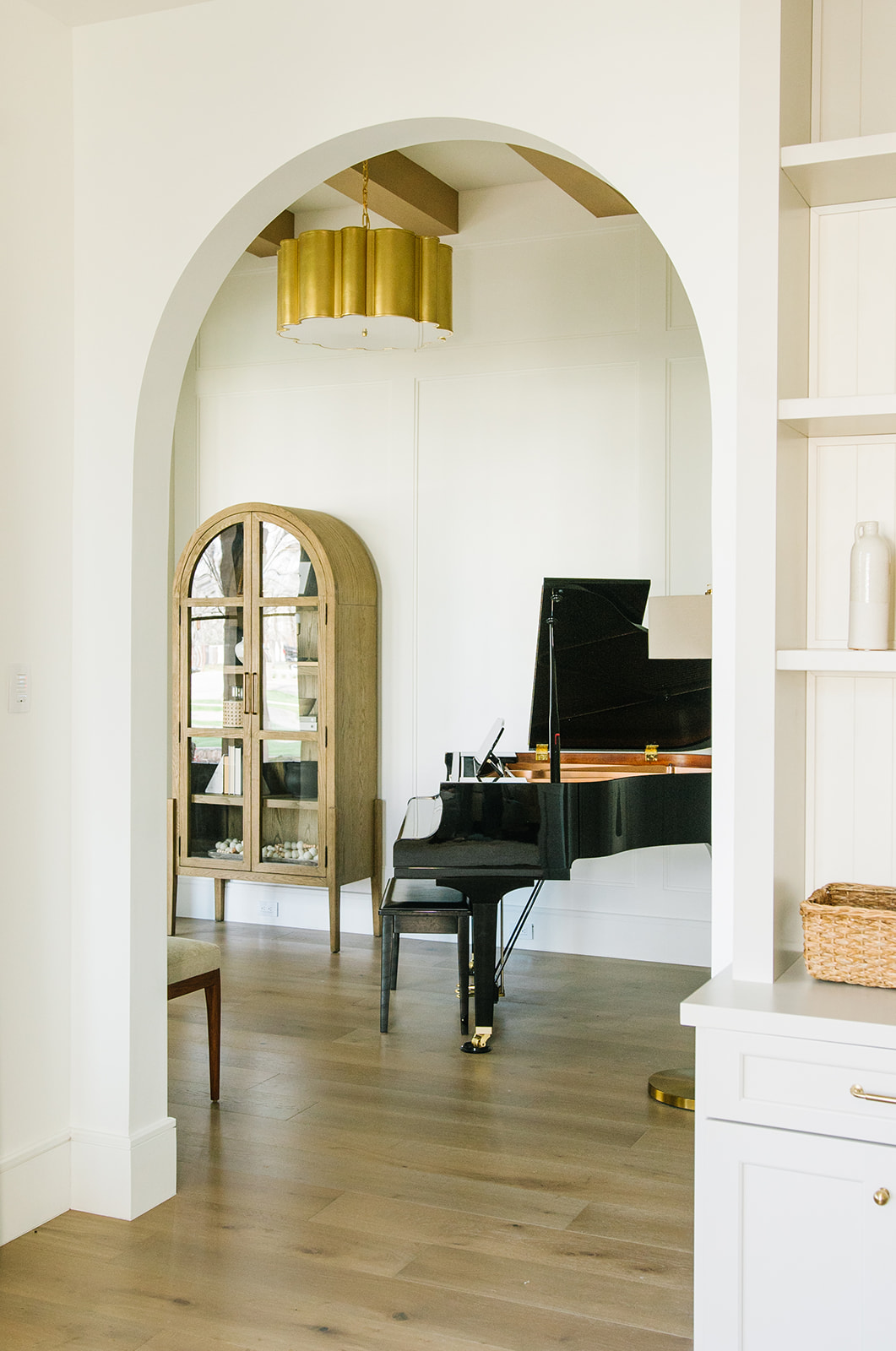 Luxury Music Room with Grand Piano and Arched Display Cabinet – A refined music room featuring a black grand piano, arched wood display cabinet, and modern gold chandelier, enhancing the elegant ambiance.