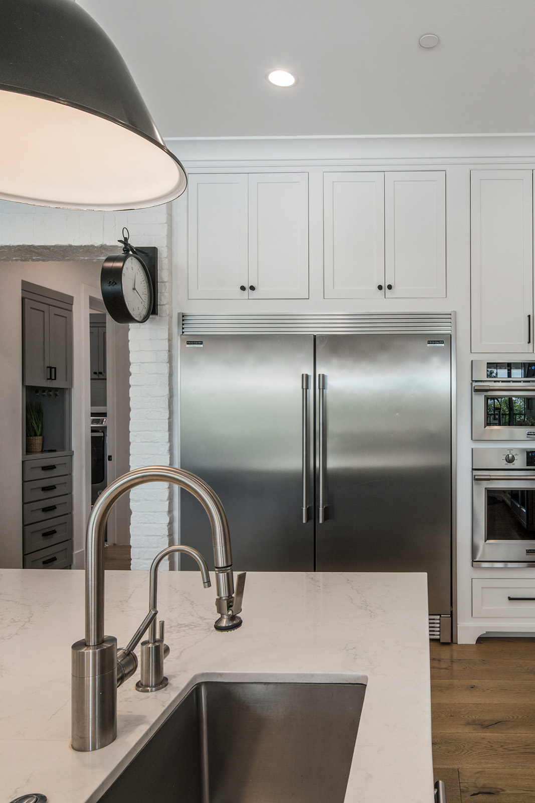 Luxury kitchen with stainless steel appliances and modern fixtures – A high-end kitchen showcasing a large stainless steel refrigerator, sleek white cabinetry, and a deep farmhouse sink with a brushed nickel pull-down faucet. The bright space is accentuated by industrial-style black pendant lighting and a minimalist design.