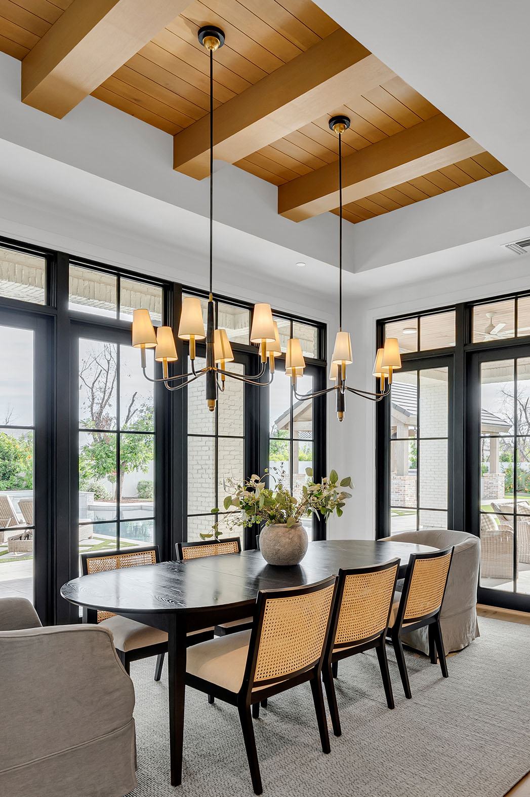Elegant Dining Room with Modern Chandeliers - A beautifully designed dining room featuring a dark wood table, woven cane dining chairs, and a black and gold chandelier, complemented by large windows and natural light.