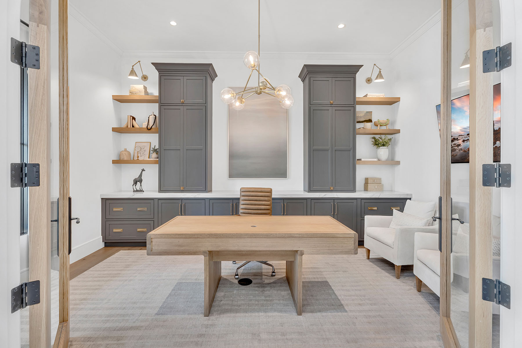 Sophisticated Home Office with Dark Cabinetry and Wooden Desk – A stylish home office with navy built-in cabinets, a sleek wooden desk, and a contemporary chandelier. A large abstract painting adds artistic flair, creating an elegant and productive workspace.