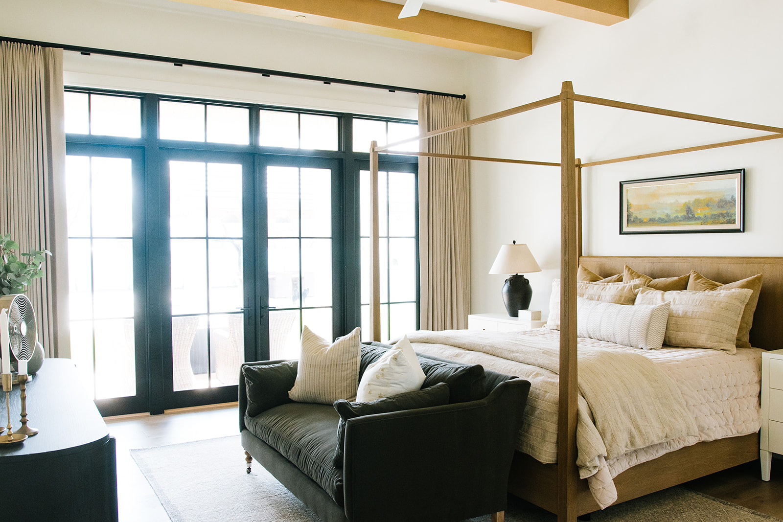 Bright Bedroom with Floor-to-Ceiling Windows – A beautifully designed bedroom with large black-framed glass doors, a wooden canopy bed, and natural textures, seamlessly blending indoor and outdoor living.