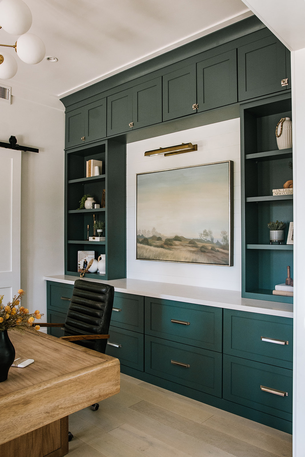 Custom Home Office with Built-in Green Cabinetry and Artwork – A sophisticated home office featuring deep green built-in cabinetry, brass hardware, and a centered landscape painting, blending luxury interior design with functional workspace solutions.