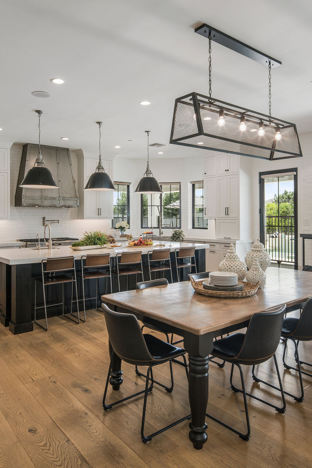 A contemporary kitchen with a large island, black industrial lighting, and a mix of rustic and modern decor.