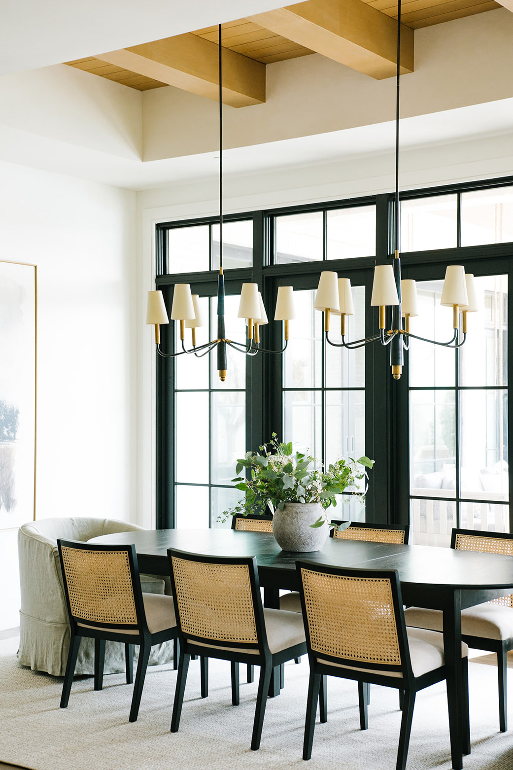 Elegant Dining Room with Modern Chandeliers - A beautifully designed dining room featuring a dark wood table, woven cane dining chairs, and a black and gold chandelier, complemented by large windows and natural light.