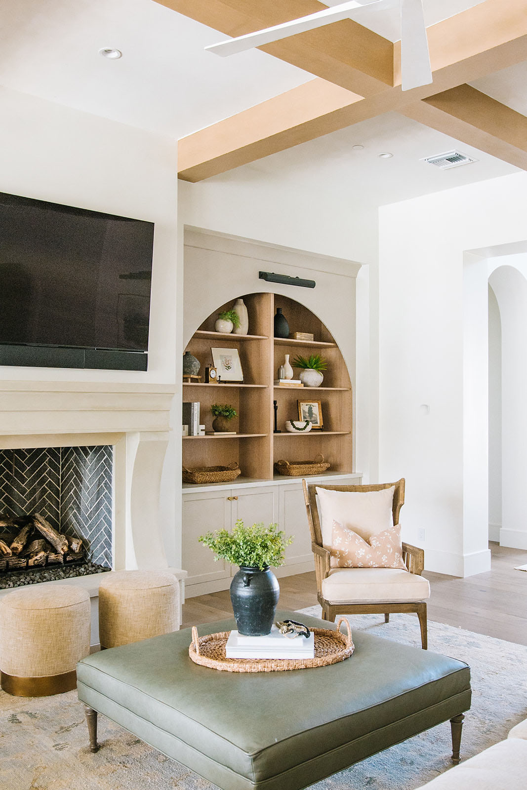 A warm and inviting living room with an arched built-in bookcase, neutral decor, and a stylish fireplace centerpiece.