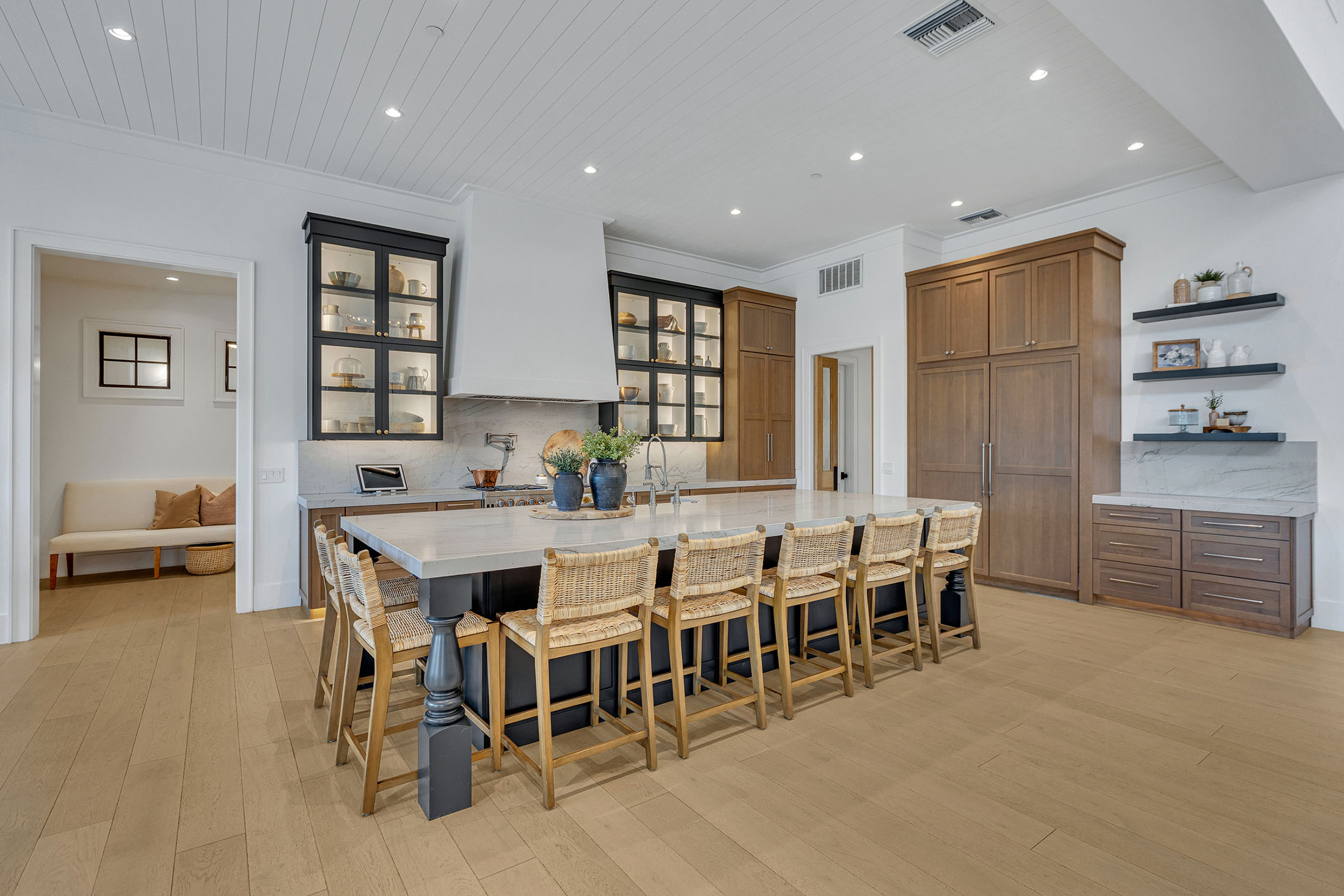 Luxury Modern Kitchen with Large Island and Custom Cabinetry – A spacious high-end kitchen featuring a large marble island with rattan bar stools, custom black and wood cabinetry, and open shelving for a modern farmhouse aesthetic.