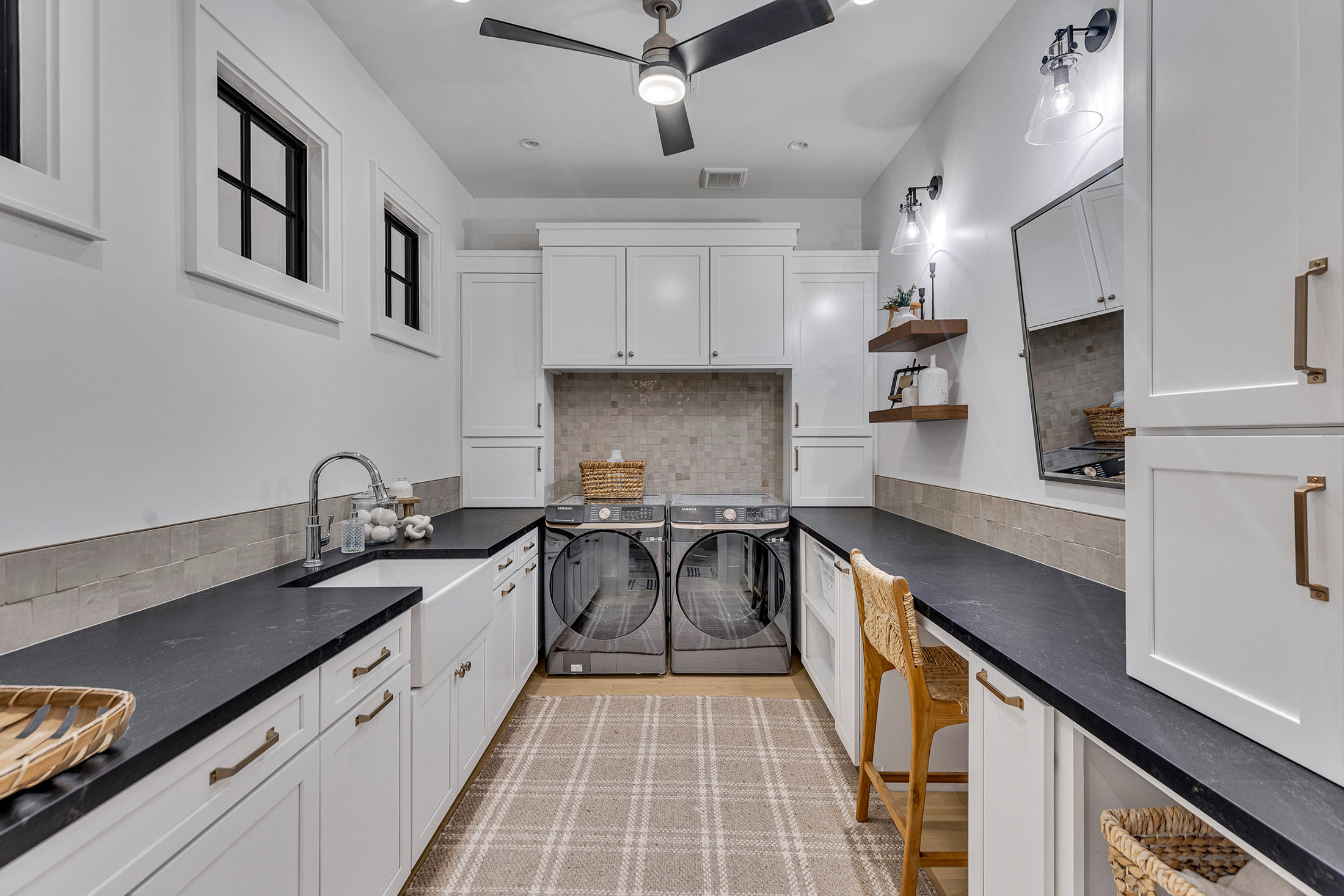 Spacious Laundry Room with White Cabinetry and Black Countertops – A functional and stylish laundry room featuring custom white cabinetry, black countertops, and modern shelving. The well-lit space includes a built-in washer and dryer setup with ample storage, ideal for home organization solutions.