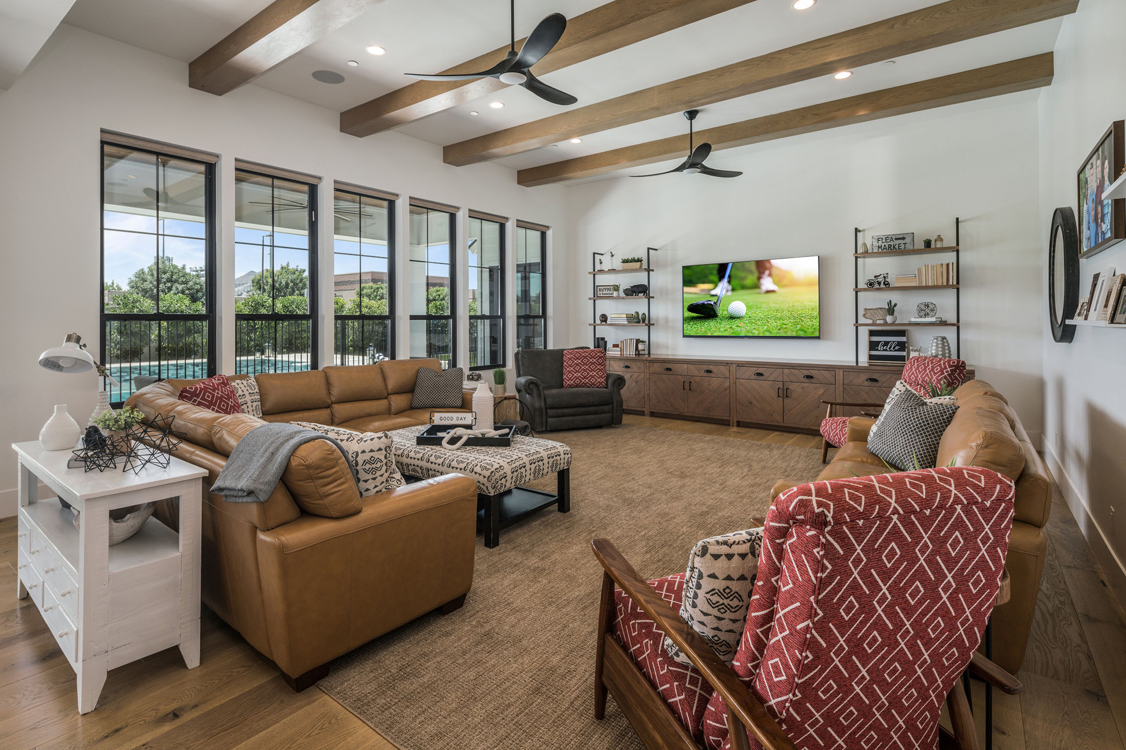 Cozy Family Room with Leather Sectional and Poolside Views – A bright and open family room featuring a large leather sectional, accent chairs with patterned upholstery, and a wall-mounted TV. Floor-to-ceiling windows provide a stunning view of the backyard pool area.