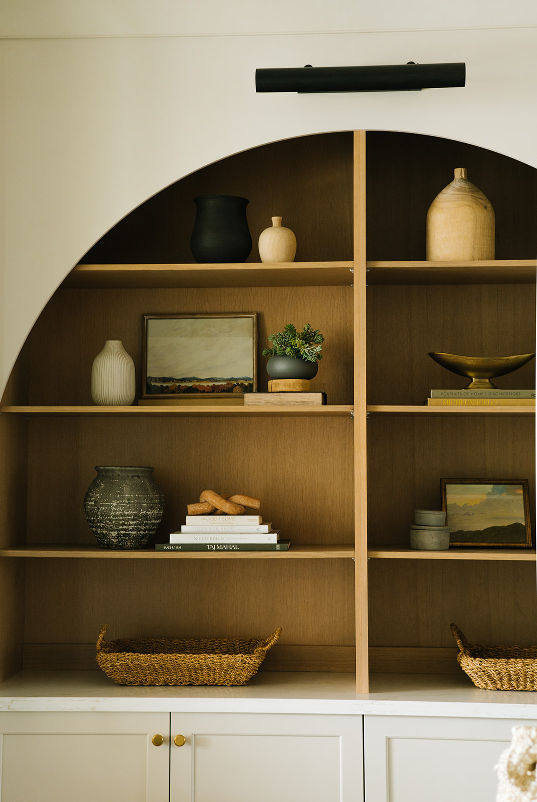 Close-Up of Decorative Arched Built-In Shelving in Living Room – A detailed view of styled arch shelving featuring earthy-toned ceramics, books, framed artwork, and woven baskets, complementing the modern farmhouse interior design.