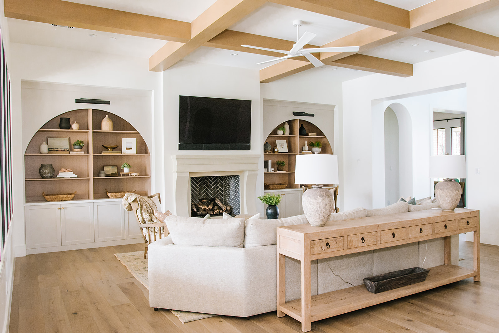 Elegant Living Room with Fireplace and Built-In Arch Shelves – A cozy yet sophisticated living room featuring a white fireplace, arched built-in shelves with decorative elements, and a plush neutral-toned sectional. Wooden ceiling beams add a rustic charm.