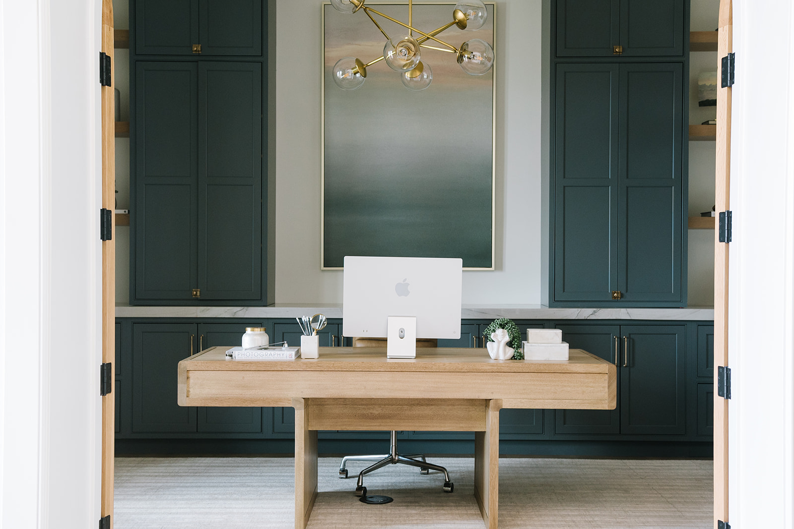 Sophisticated Home Office with Dark Cabinetry and Wooden Desk – A stylish home office with navy built-in cabinets, a sleek wooden desk, and a contemporary chandelier. A large abstract painting adds artistic flair, creating an elegant and productive workspace.