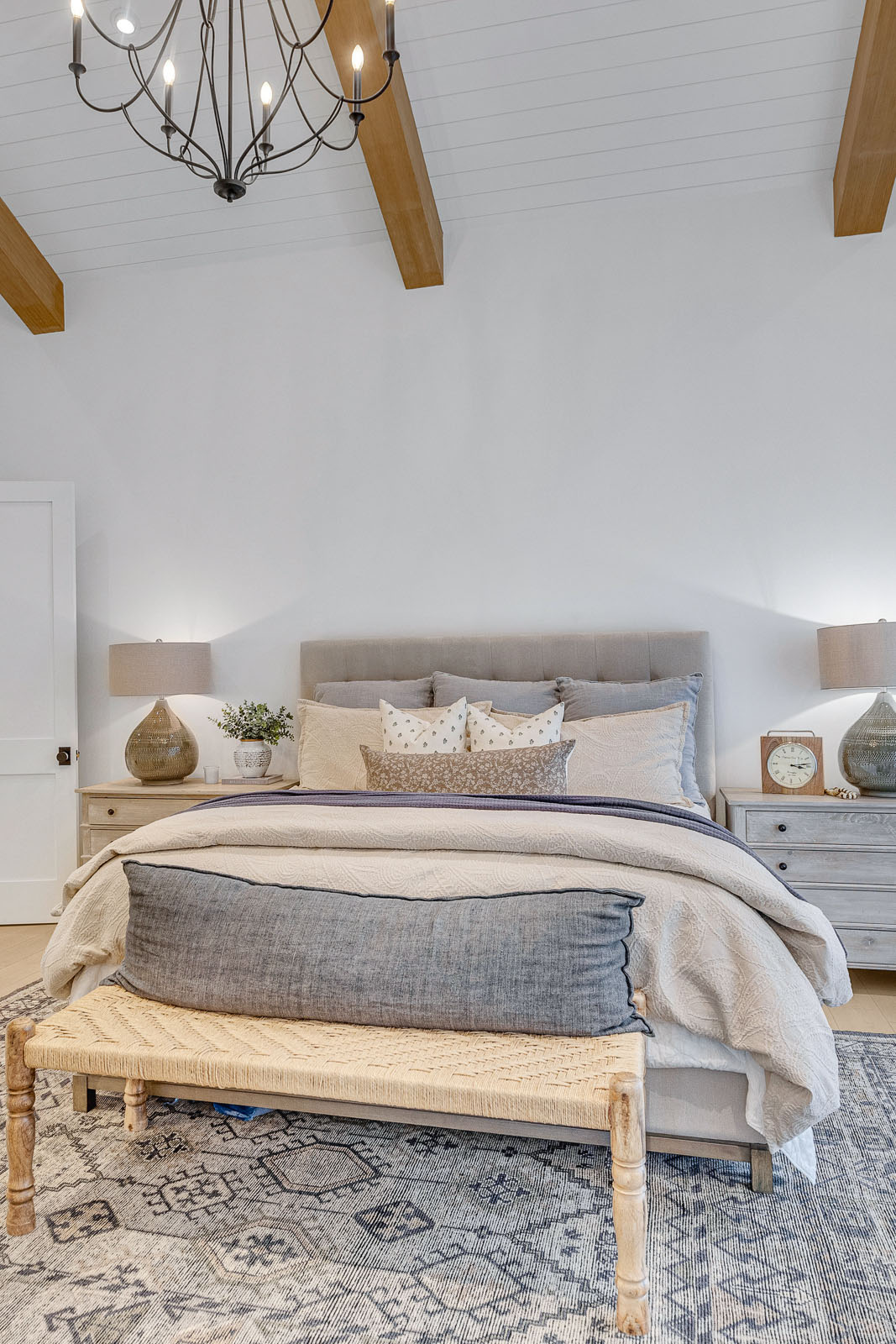 Elegant Master Bedroom with Vaulted Ceilings and Chandelier – Luxurious master bedroom featuring exposed wood beams, a stunning black iron chandelier, and cozy neutral-toned bedding, creating a sophisticated and inviting retreat.