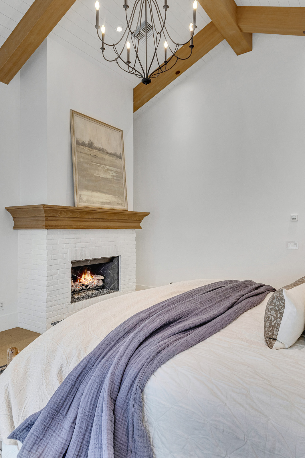 Cozy Bedroom with Fireplace and Rustic Charm – Stylish master bedroom with a white brick fireplace, a rustic wood mantel, and soft neutral decor, offering a warm and inviting ambiance for relaxation.