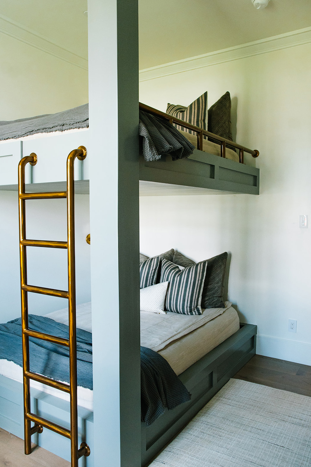 Custom Built-in Bunk Beds with Brass Ladder – Stylish built-in bunk beds painted in muted green, featuring a brass ladder and cozy striped pillows for a modern farmhouse bedroom design.