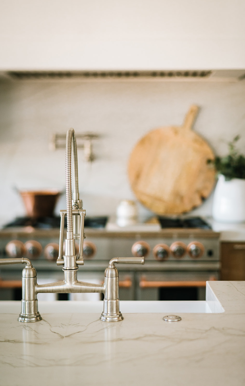 Luxury Kitchen with Farmhouse-Style Bridge Faucet – Close-up of a high-end brushed nickel bridge faucet set against a marble countertop and a gourmet gas range with copper accents, highlighting timeless craftsmanship in kitchen design.