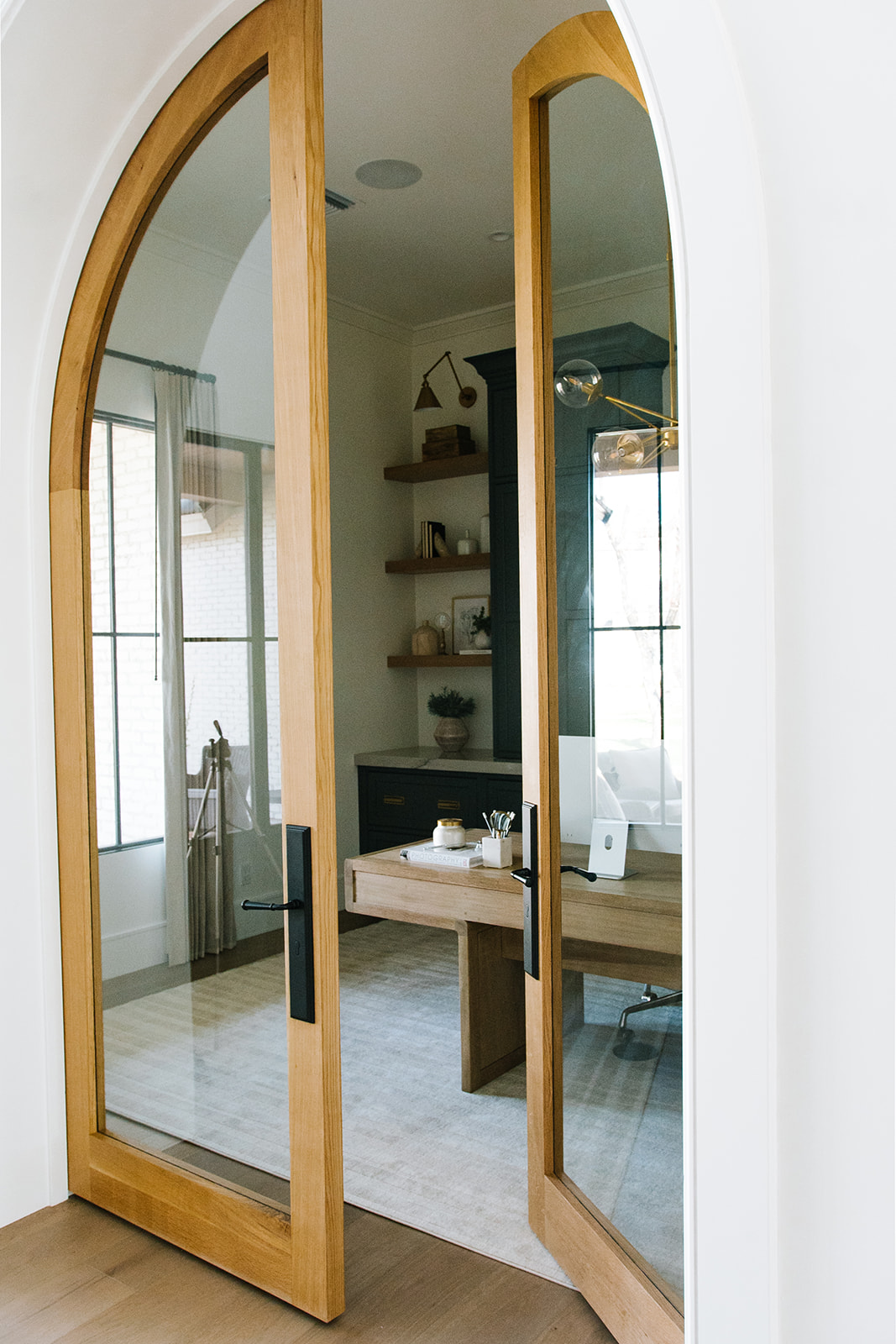 Elegant Home Office with Arched Glass Doors – A stylish home office featuring arched glass double doors with natural wood frames, dark built-in cabinetry, and modern decor for a sophisticated workspace.