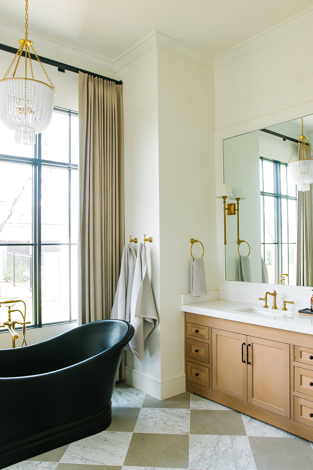 Luxury Bathroom with Black Freestanding Tub and Gold Accents – Elegant bathroom featuring a black freestanding bathtub, gold fixtures, marble checkerboard flooring, and large windows for natural light.