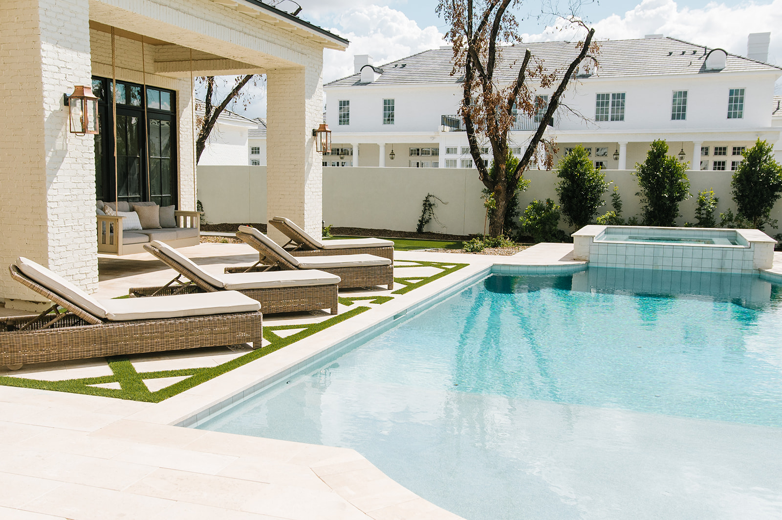 Luxury Backyard with Pool, Spa, and Lounge Seating – Beautiful outdoor space with a sparkling pool, spa, and cushioned lounge chairs, framed by a covered patio with a porch swing and lush landscaping.