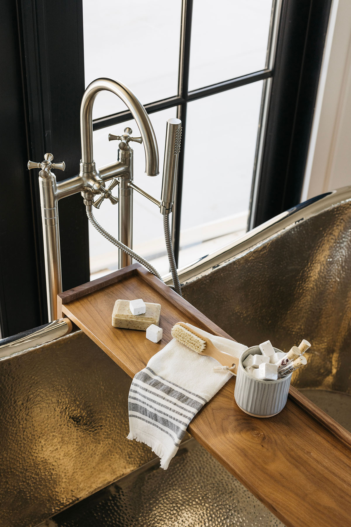 Luxury Freestanding Bathtub with Spa-Like Bath Accessories – A high-end bathroom detail showcasing a freestanding metallic tub, a wooden bath tray with artisanal soap and bath salts, and a classic gooseneck faucet, creating a spa-inspired retreat in a custom home.