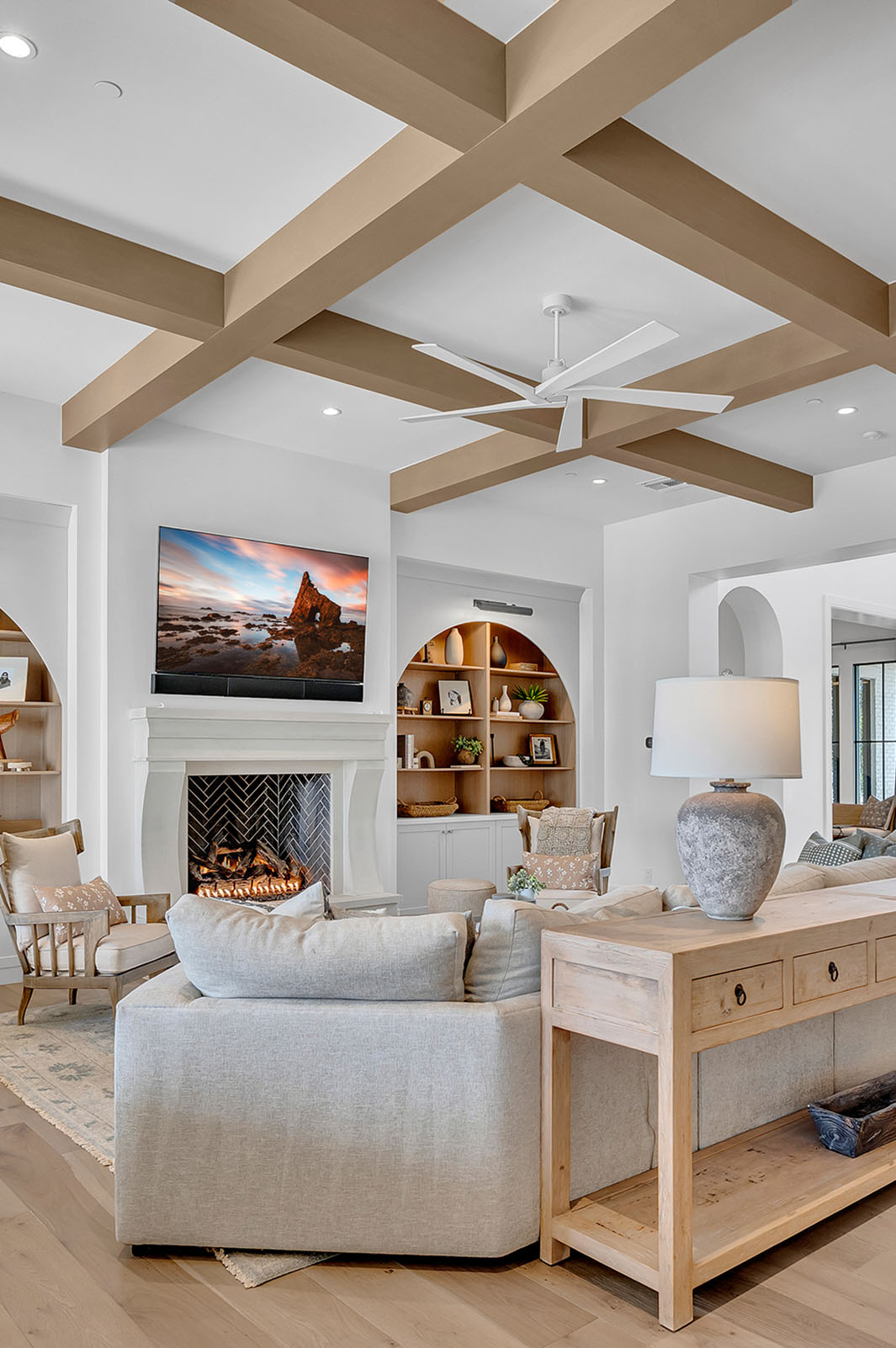 Elegant living space featuring a custom-built arched wood bookcase with warm tones, styled with curated decor and natural elements. The room showcases exposed ceiling beams, a cozy neutral-toned sofa, and layered textures, blending rustic charm with modern sophistication for a timeless aesthetic.